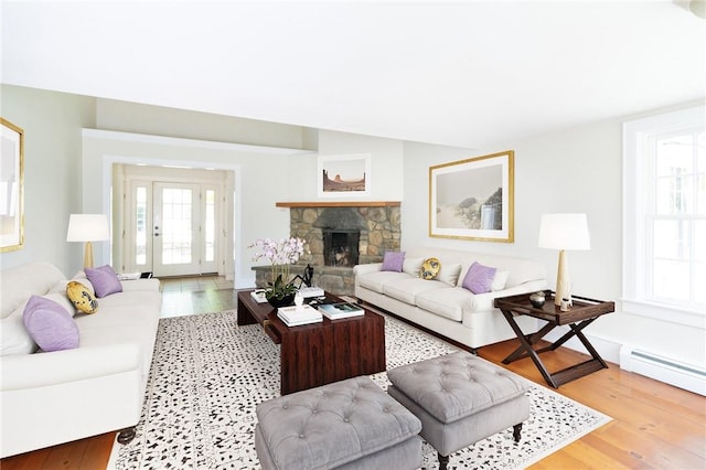 living room featuring light hardwood / wood-style floors, baseboard heating, a fireplace, and a wealth of natural light