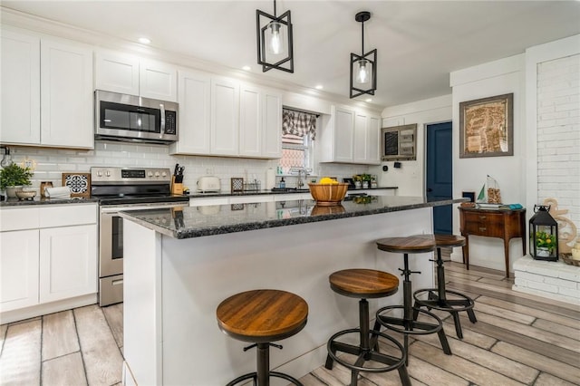 kitchen featuring white cabinetry, hanging light fixtures, stainless steel appliances, light hardwood / wood-style floors, and a kitchen island