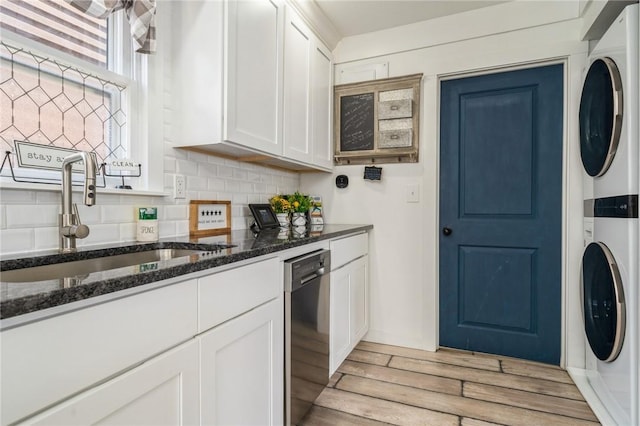 kitchen with stacked washer / dryer, dishwasher, sink, and white cabinets