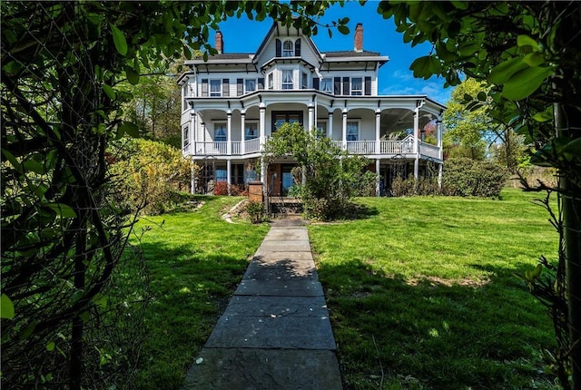 victorian house with a balcony, a front yard, and covered porch