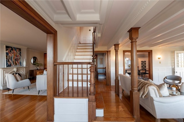 stairway featuring decorative columns, wood-type flooring, ornamental molding, and beam ceiling