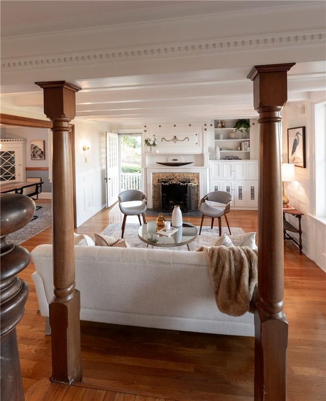 living room featuring wood-type flooring, ornamental molding, a premium fireplace, and ornate columns