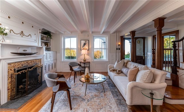 living room featuring beam ceiling, a premium fireplace, ornate columns, and light wood-type flooring