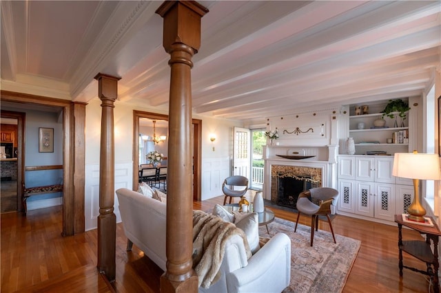 living room featuring ornate columns, a fireplace, beamed ceiling, wood-type flooring, and crown molding