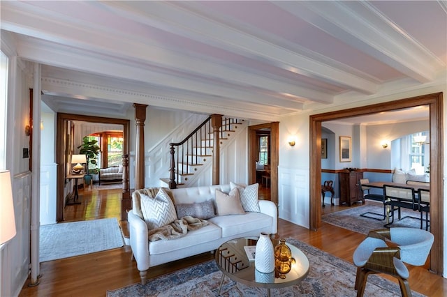 living room featuring ornamental molding, wood-type flooring, decorative columns, and beamed ceiling