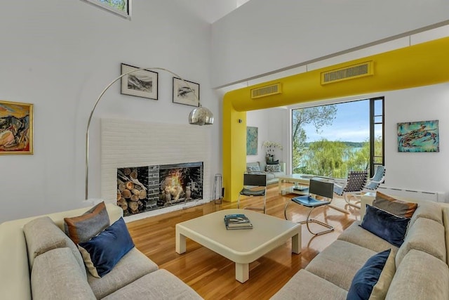 living room with a high ceiling, hardwood / wood-style flooring, a brick fireplace, and a baseboard heating unit