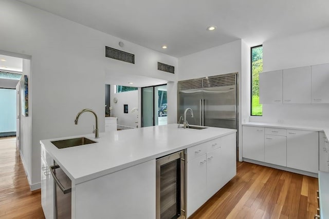 kitchen featuring a center island with sink, sink, wine cooler, light hardwood / wood-style floors, and stainless steel appliances