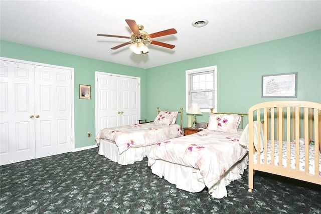 bedroom with ceiling fan, dark carpet, and multiple closets