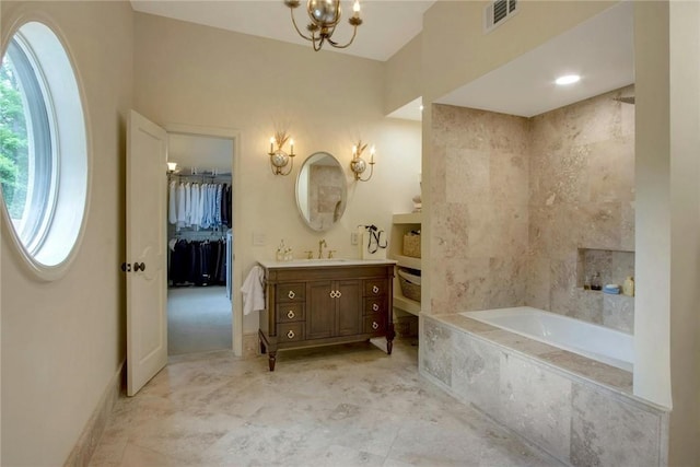 bathroom featuring tiled tub, vanity, and a chandelier