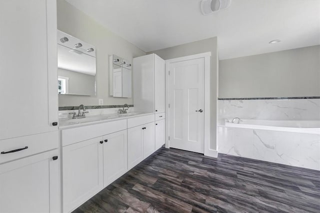 bathroom with hardwood / wood-style flooring, vanity, and tiled bath