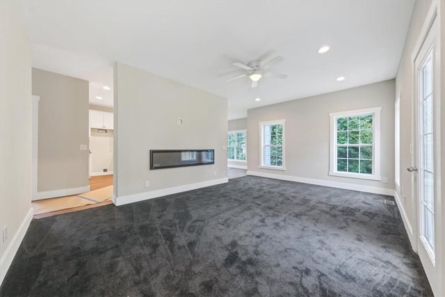 unfurnished living room with dark colored carpet and ceiling fan