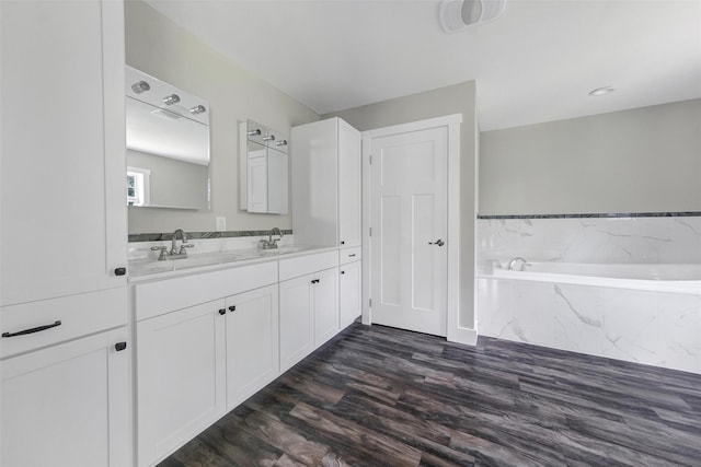 bathroom with hardwood / wood-style floors, a relaxing tiled tub, and vanity