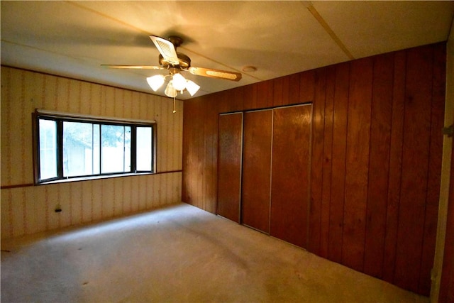 unfurnished bedroom with carpet, ceiling fan, wooden walls, and a closet