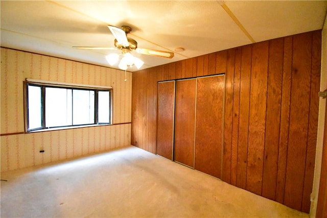 unfurnished bedroom featuring carpet floors, a closet, ceiling fan, and wooden walls