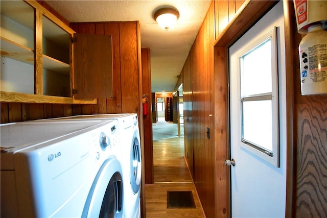 laundry area with a textured ceiling, hardwood / wood-style flooring, washer and clothes dryer, and wood walls