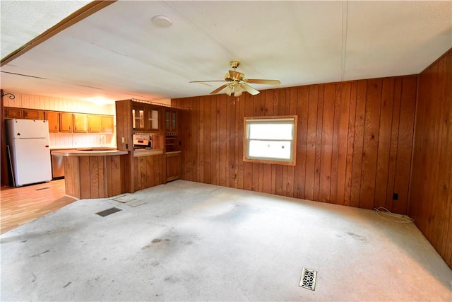 unfurnished living room featuring wood walls, ceiling fan, and light carpet