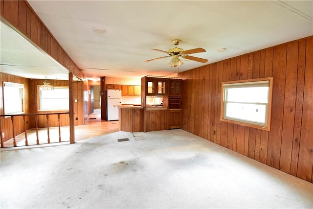 unfurnished living room with wood walls, a healthy amount of sunlight, and ceiling fan with notable chandelier