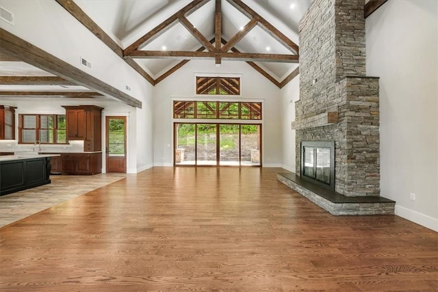 unfurnished living room with beamed ceiling, light hardwood / wood-style flooring, high vaulted ceiling, and a stone fireplace