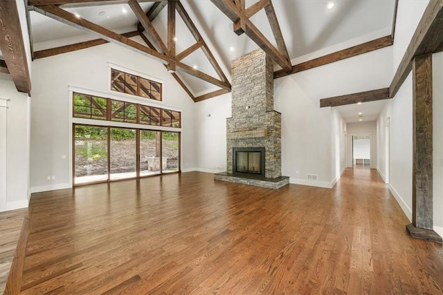 unfurnished living room featuring a stone fireplace, beamed ceiling, high vaulted ceiling, and wood-type flooring