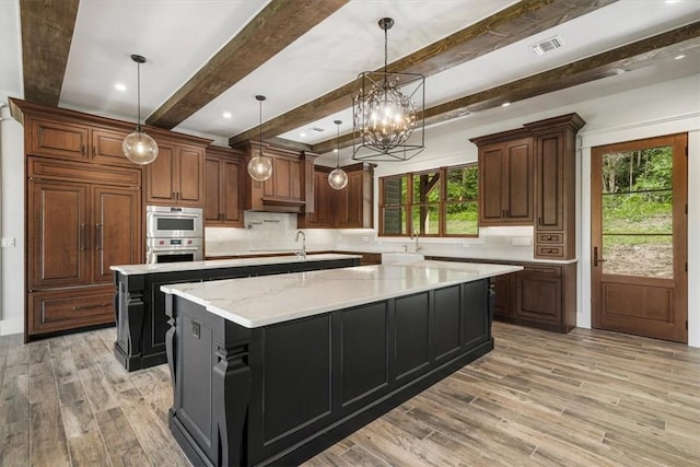 kitchen featuring a healthy amount of sunlight, a spacious island, beam ceiling, and hanging light fixtures