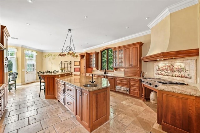 kitchen featuring a kitchen breakfast bar, premium range hood, crown molding, an island with sink, and decorative light fixtures