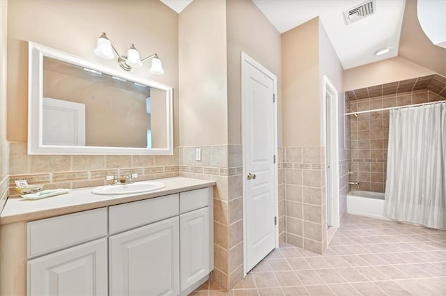 bathroom with vanity, shower / bath combo, vaulted ceiling, tile patterned flooring, and tile walls