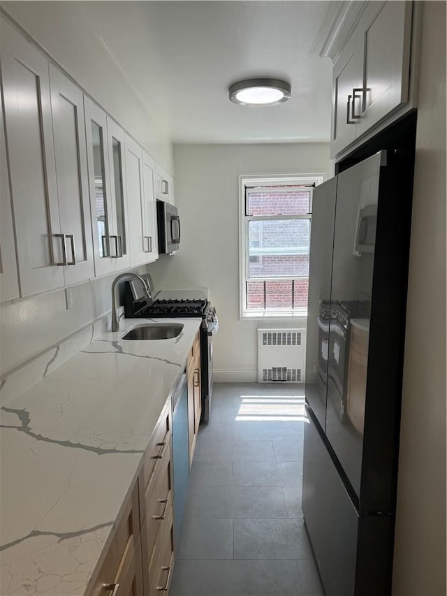 kitchen with light stone counters, radiator heating unit, white cabinets, and stainless steel appliances