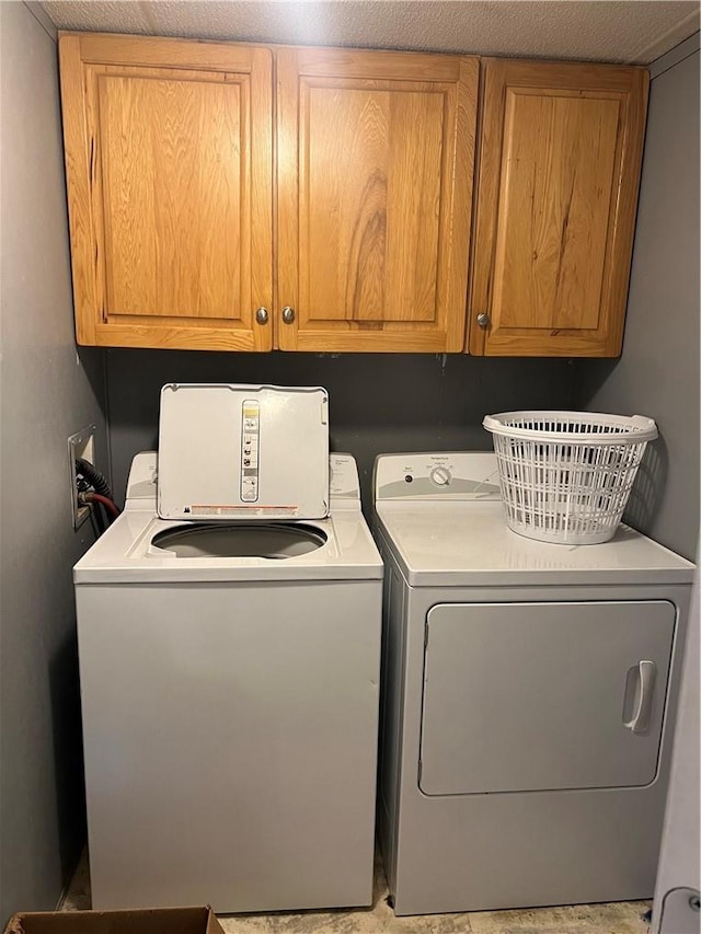 clothes washing area with washing machine and dryer, cabinets, and a textured ceiling