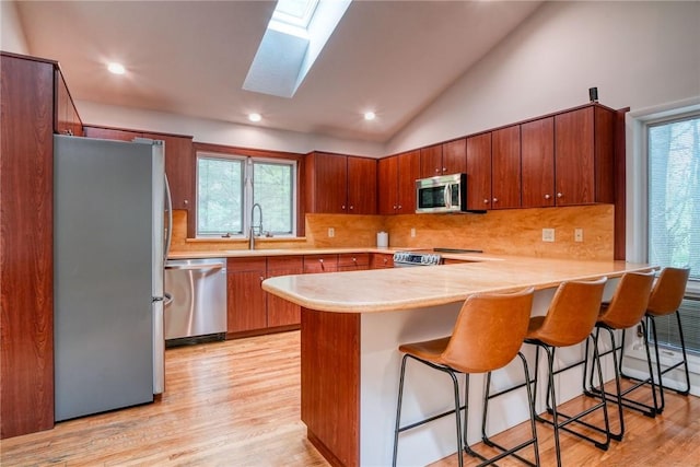 kitchen with kitchen peninsula, appliances with stainless steel finishes, lofted ceiling with skylight, and a healthy amount of sunlight