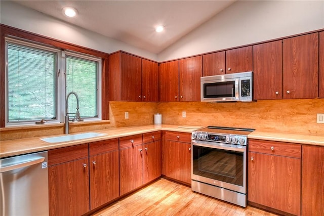 kitchen featuring backsplash, stainless steel appliances, vaulted ceiling, sink, and light hardwood / wood-style flooring