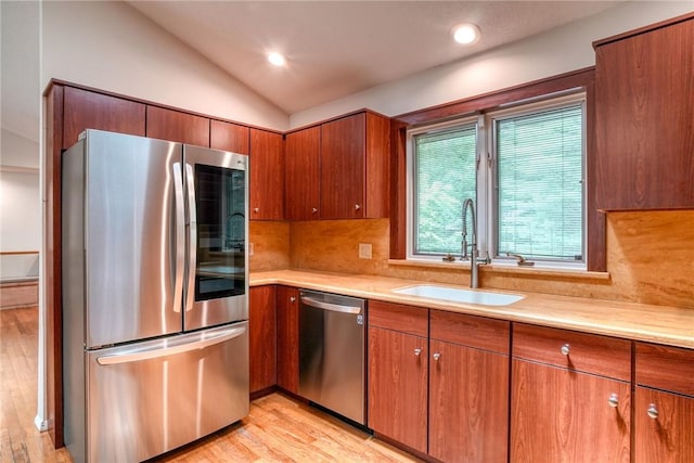 kitchen featuring backsplash, stainless steel appliances, vaulted ceiling, sink, and light hardwood / wood-style floors