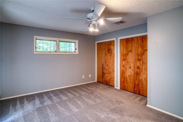 unfurnished bedroom featuring carpet, a textured ceiling, two closets, and ceiling fan