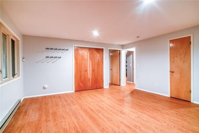 unfurnished bedroom featuring light hardwood / wood-style floors, multiple closets, and a baseboard heating unit