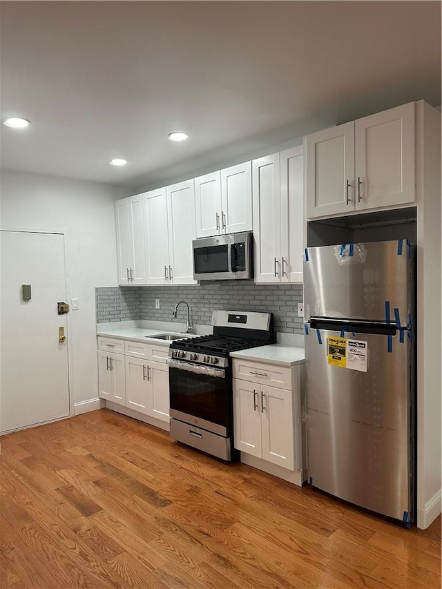 kitchen featuring decorative backsplash, appliances with stainless steel finishes, sink, light hardwood / wood-style flooring, and white cabinets