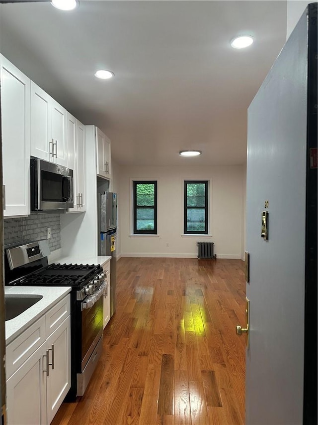 kitchen featuring radiator, stainless steel appliances, decorative backsplash, white cabinets, and light wood-type flooring