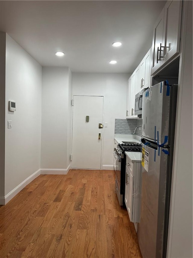 kitchen with white cabinets, decorative backsplash, stainless steel appliances, and light hardwood / wood-style floors