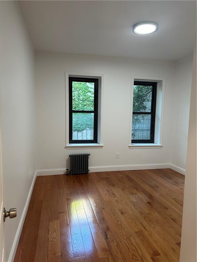 empty room with hardwood / wood-style floors, plenty of natural light, and radiator heating unit