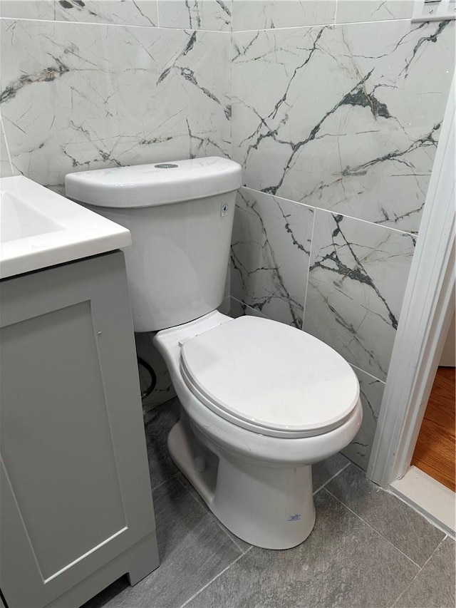 bathroom featuring vanity, toilet, and tile walls