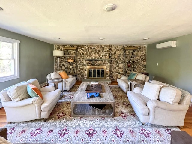 living room featuring a wall mounted air conditioner, hardwood / wood-style flooring, and a stone fireplace