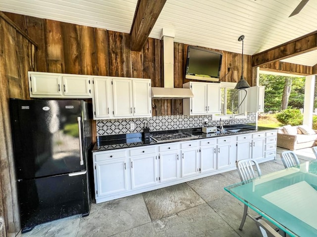 kitchen featuring pendant lighting, black refrigerator, white cabinets, and wooden walls