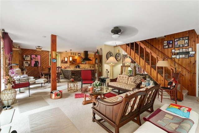 living room with wooden walls, ceiling fan, and light colored carpet