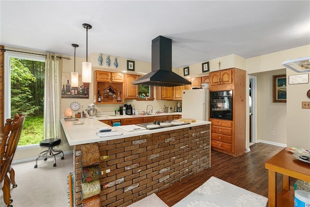 kitchen featuring hanging light fixtures, kitchen peninsula, island exhaust hood, white fridge, and black oven