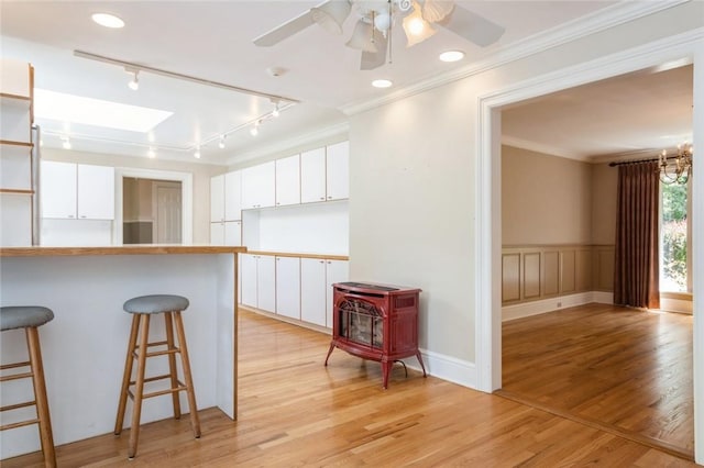 kitchen featuring a kitchen bar, light wood-type flooring, track lighting, ornamental molding, and white cabinets