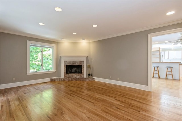 unfurnished living room featuring a premium fireplace, crown molding, ceiling fan, and light wood-type flooring