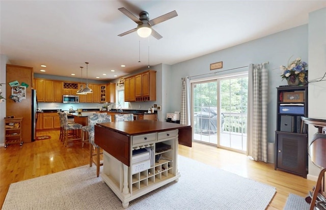 kitchen featuring ceiling fan, appliances with stainless steel finishes, pendant lighting, a kitchen island, and light wood-type flooring