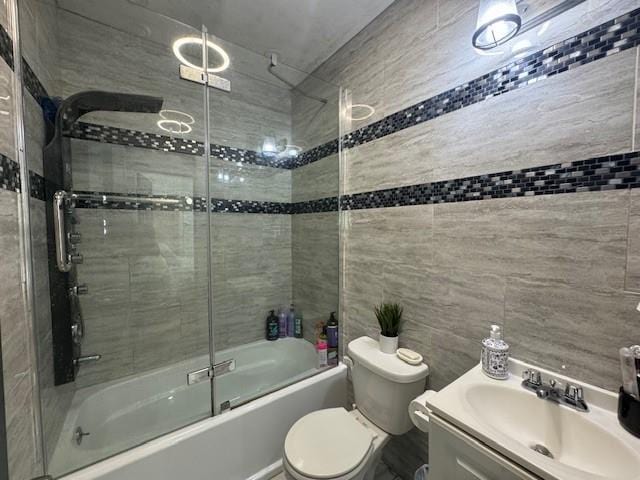 full bathroom with vanity, toilet, bath / shower combo with glass door, and tile walls