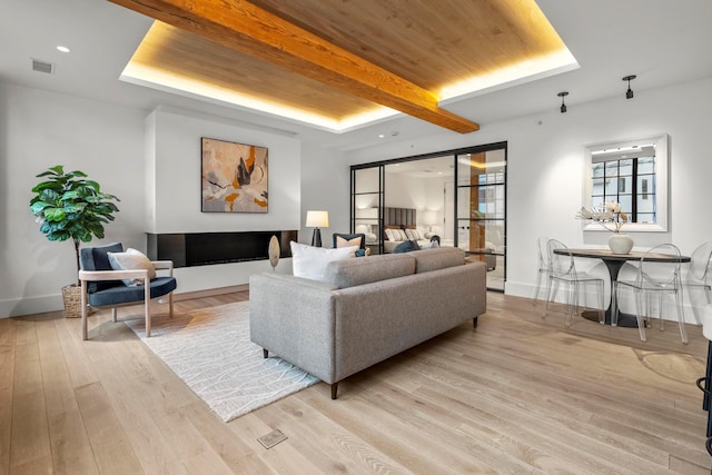 living room featuring beamed ceiling, wooden ceiling, a tray ceiling, and light wood-type flooring