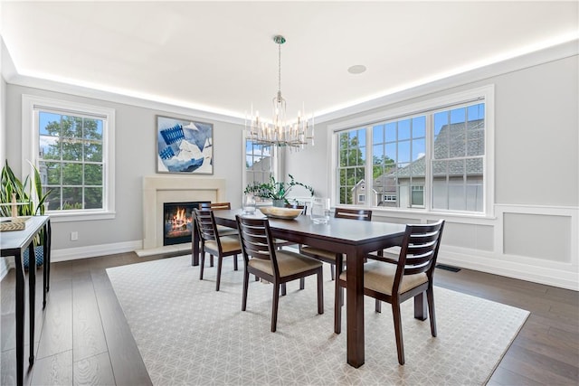 dining space with a notable chandelier, a healthy amount of sunlight, crown molding, and dark wood-type flooring