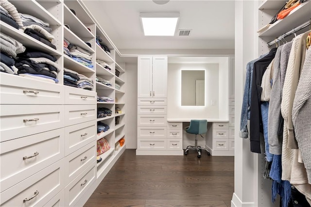 spacious closet featuring dark hardwood / wood-style flooring and built in desk