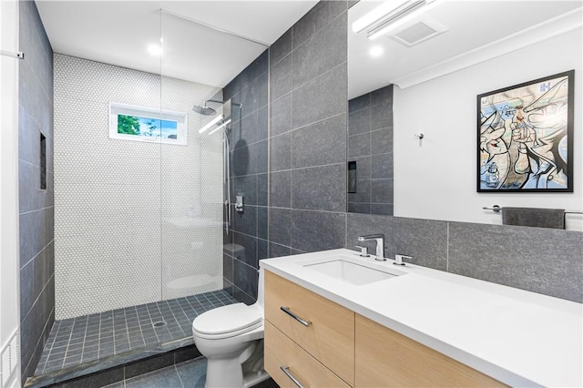 bathroom with vanity, tile patterned flooring, toilet, tile walls, and a tile shower